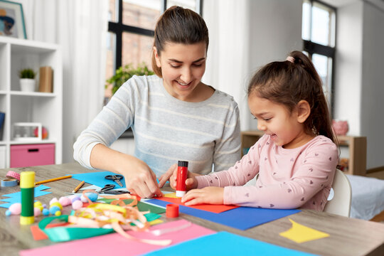 family, art and craft concept - mother spending time with her little daughter with glue making applique of color paper at home