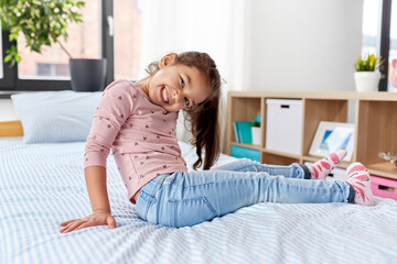 people and childhood concept - happy smiling little girl sitting on bed at home