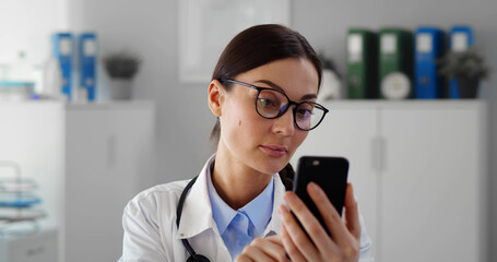 Happy female doctor using smartphone in medical office