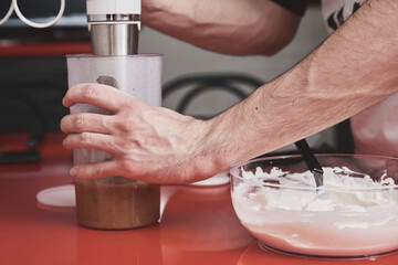 Unrecognizable young caucasian man in apron washing using a blender in a kitchen. He is preparing a cake.