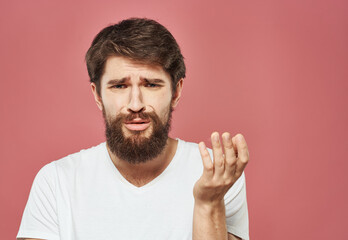 Naklejka premium Portrait of an upset man in a white t-shirt on a pink background cropped view