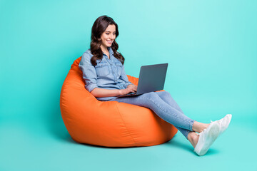 Photo of adorable pretty young lady dressed denim shirt sitting beanbag typing modern gadget isolated teal color background