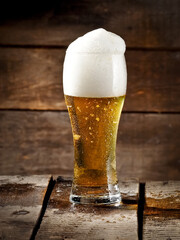 Cold beer glass with froth head on wood