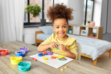childhood, creativity and hobby concept - little african american girl with modeling clay playing at home