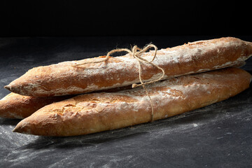 food, baking and cooking concept - pile of baguette bread loaves tied with rope on table over dark background