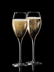 Two full champagne glasses with bubbles on black background