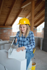 pretty young female bricklayer with yellow safety helmet is sawing bricks on a construction site in the house, concept female workers