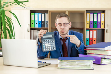 Naklejka premium Accountant businessman at his desk in the office shows a finger on a calculator. Financial check. Preparation of a report by an office worker.