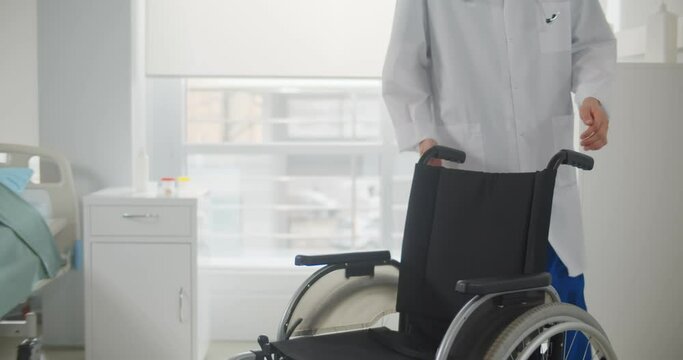 Male nurse pushing an empty wheelchair in hospital ward