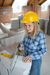 pretty young female bricklayer with yellow safety helmet is sawing bricks on a construction site in the house, concept female workers