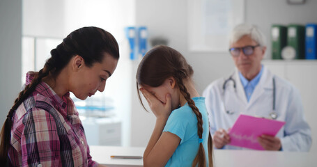 Obraz premium Portrait of mother comforting cute little girl crying at doctor office