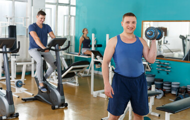 Fototapeta na wymiar Portrait of man in sportswear lifting dumbbells at gym
