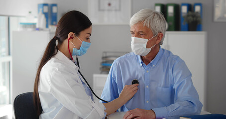Close up serious doctor wearing mask checking senior patient lungs with stethoscope