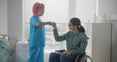 Smiling female nurse and male patient in wheelchair sharing secret hand gesture