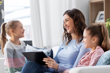 people, family and technology concept - happy mother and two daughters with tablet pc computer at home