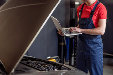 Auto mechanic hands with laptop near open hood