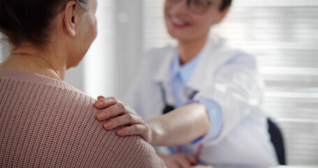Female doctor holding aged patient by shoulder soothing her fear