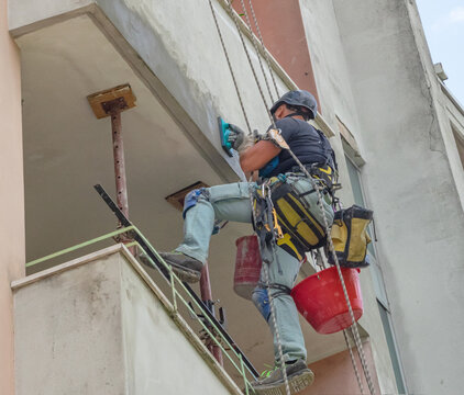 bricklayer suspended with ropes repairs facade building