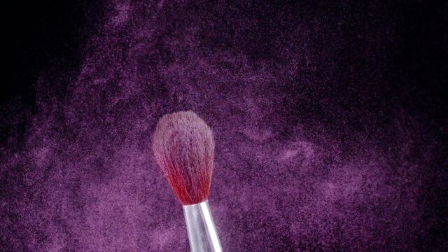 Makeup brush shudders and creates a swirl of fine particles of pink powder against a black background, slow motion, 300fps.