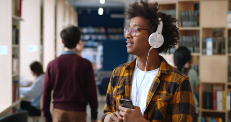 African student enjoying music in headphones dancing in school library