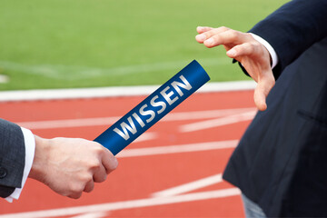 Businessmen passing baton in relay race with German word Wissen means Knowledge 