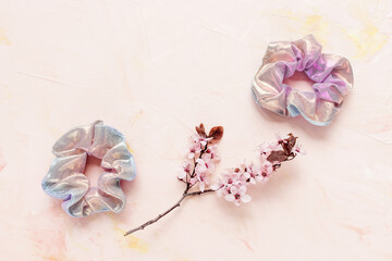 Twoshiny scrunchies and fresh spring branch with pink flowers on pastel backround. Flat lay, top view. Diy accessories, hairstyle, lifestyle, spring and summer outfit ideas concept, copy space