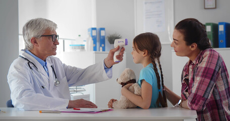 Obraz premium Friendly doctor talking with young woman and daughter measuring temperature with infrared thermometer