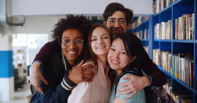Portrait of happy multiethnic young people posing at camera in school library