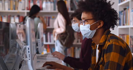 African male student in safety mask working on computer in public library