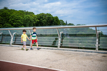 Portrait of two boys kid a walk over a bridge and looking down, child walking outside in sunny day, Young boys relaxing outdoors in summer on glass bridge. Tourism concept