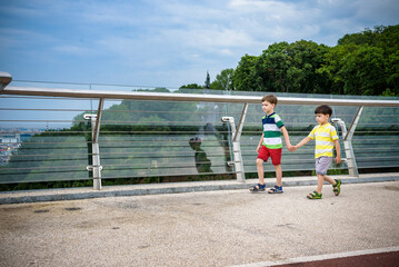 Portrait of two boys kid a walk over a bridge and looking down, child walking outside in sunny day, Young boys relaxing outdoors in summer on glass bridge. Tourism concept