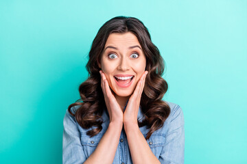 Photo of tricky shocked young woman wear jeans shirt arms cheeks open mouth smiling isolated turquoise color background