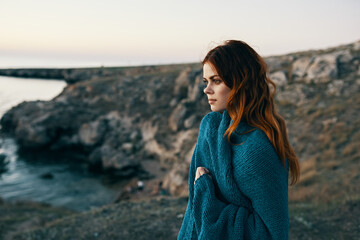 woman at sunset near the sea in the mountains with a blanket on her shoulders