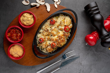 Baked champignons mushrooms, with cheese, parsley and roasted garlic in black bowl.