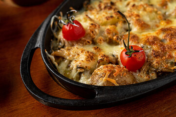 Baked champignons mushrooms, with cheese, parsley and roasted garlic in black bowl.