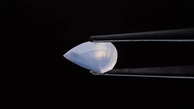 natural opal gemstone in the tweezer on the background