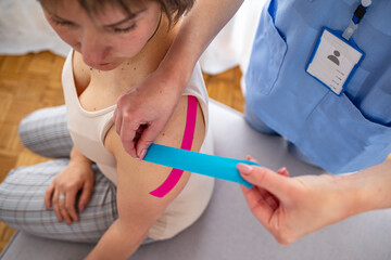 Female physiotherapist applying tape on a female patient. Shoulder treatment with kinesio tape....