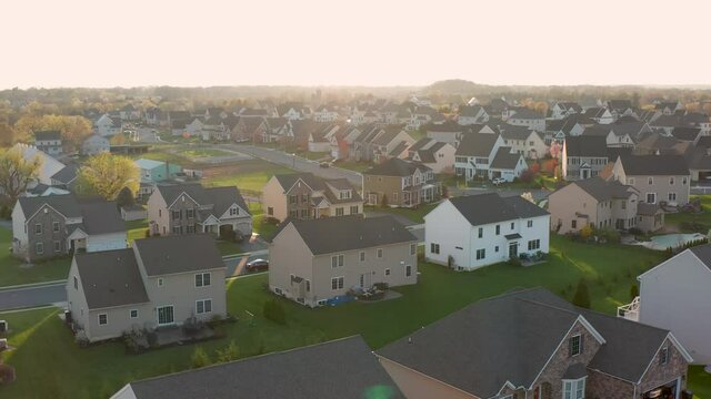 Aerial of large new homes in USA during spring season. Colorful trees bloom at sunset, sunrise. Backyard open green space in residential neighborhood development.
