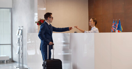 Man with suitcase in hotel check out at reception or front office