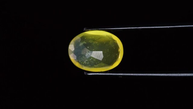 natural yellow fire opal gemstone in the tweezer on the background