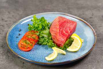 Raw tuna steak with salad and lemon on blue plate. Fish diet.