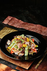 salad with ham, orange slices, tomato, cucumber and lettuce leaves in a black plate on a copper background. 