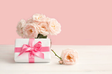 Tender light garden roses in a transparent vase and gift box on pink pastel background.