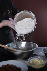 The pastry chef kneads the dough for baking. Flour is poured out of a metal bowl. Vertical photo. An unrecognizable person.