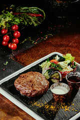 grilled meat patty with salad and two sauces on a black plate on a copper background.