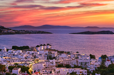 Fototapeta premium Beautiful sunset view of famous traditional white windmills on hilltop, Mykonos, Greece. Whitewashed house, colorful sunset sky, summer, town light on
