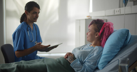 Young male doctor and female patient talking in hospital ward