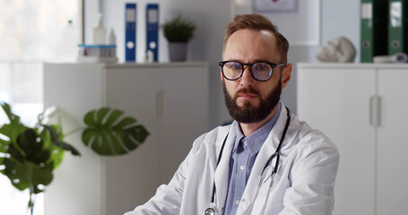 Portrait of pensive caucasian male doctor looking at camera in clinic office