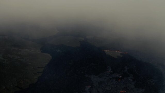 Flying through volcanic smoke, overlooking lava fields at a volcano basin - Aerial drone view