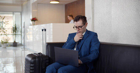 Young businessman using laptop sitting in modern hotel lobby